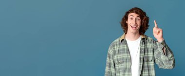 Yaratıcı bir fikir. Neşeli milenyum adamı turkuaz arka planda EUREKA jesti gösteriyor