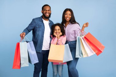 Kara Cuma Satışı. Afro-Amerikan üç neşeli insanın portresi yeni kıyafetler ve hediyelerle dolu alışveriş çantaları, aile alışverişi, kameraya poz verme, mavi turkuaz stüdyo duvarı