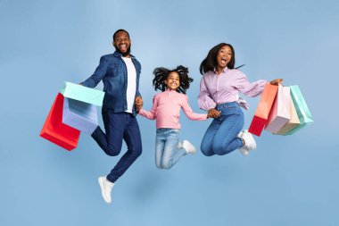 Birlikte alışveriş yapmak. Havada zıplayan, Turkuaz Stüdyo 'nun arka planında izole edilmiş bir sürü parlak alışveriş torbası taşıyan heyecanlı üç Afrikalı Amerikalı ailenin el ele tutuşması.