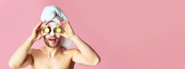 Yüzünde nemlendirici maske olan komik bir adam, gözüne salatalık koyar.