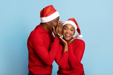 Kırmızı süveter ve Noel Baba şapkaları giymiş neşeli siyah bir çift, neşeli bir anı paylaşıyor. Bir fısıltıyla, festival sezonunda açık mavi bir zemin ile çevrili..