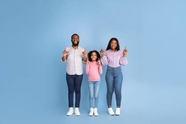 Mavi arka planda duran üç kişilik neşeli Afro-Amerikan ailesi. Heyecanlı adam, kadın ve ergen kız bedava fotokopi alanını gösteriyorlar. Advert için Boş Yer, Tam Uzunluk