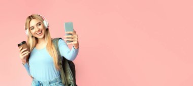 Selfie 'yi seviyorum. Kulaklıkla selfie çeken sarışın genç kızın portresi. Akıllı telefon kullanıyor, elinde kahve tutuyor, fotokopi çekiyor.