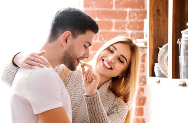 Erkek arkadaşını besleyen ve evde yemek pişirirken gülümseyen güzel bir kız arkadaş.