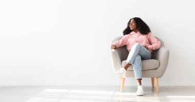 Evdeki koltukta oturmuş fotokopi odasına bakıp gülümseyen gür saçlı neşeli siyah kadın. Afro-Amerikan bir bayanın haftasonunu yalnız geçirmesi çok güzel.