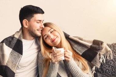 Mutlu genç adam evde sıcak ekose altında kız arkadaşına sarılıyor.