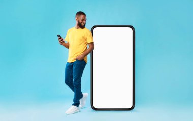 Mobil cihazlı neşeli siyahi adam mavi arka planda dev akıllı telefona bakıyor, beyaz ekranda mobil uygulama için model alıyor. Cep telefonu web sitesi şablonu, havalı online mağaza reklamı