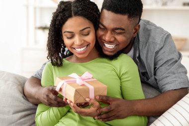 Romantik sürpriz. Sevgi dolu siyah koca, mutlu karısına evde hediye veriyor, doğum günüyle selamlıyor, arkadan sarılıyor.