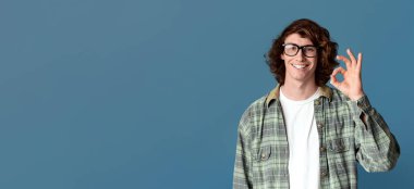 Kıvırcık milenyum çocuğu iyi bir jest yapıyor, turkuaz arka planda pozitifliğini gösteriyor.