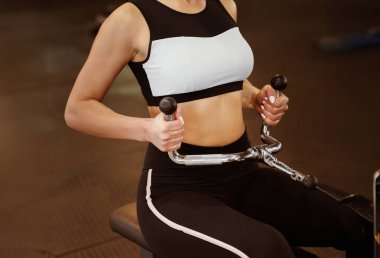 Spor kulübünde kablo ağırlık makinesiyle egzersiz yapan genç bir kadın.