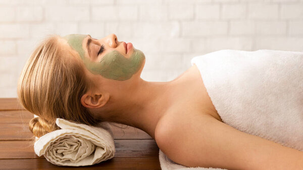 Beautiful millennial woman in spa salon with mask on her face, free space