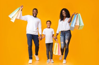 Aile alışverişi. Afrika kökenli Amerikalı aileler ve kızları alışveriş torbalarını taşıyorlar ve sarı arka planda gülümsüyorlar.
