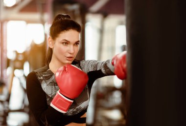 Spor ve spor. Boks eldivenli genç bir kadın spor salonunda topa vuruyor.