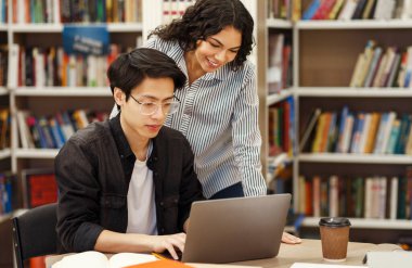 Academic Advisor. Female brazilian counselor monitoring work of korean architect student who using laptop in library