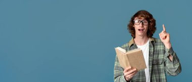 Eğitim konsepti. Kitap okuyan ve turkuaz arkaplanı işaret eden genç adam şaşırdı.