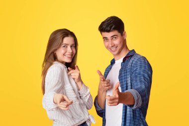 Biz yaptık ve sen de yapabilirsin. Komik şanslı bin yıllık erkek ve kadın kamerayı işaret ediyor ve iyi günde kazandıktan sonra başarıya seviniyor, sarı arka planda izole edilmiş, boş alan, stüdyo çekimi, kesilmiş,
