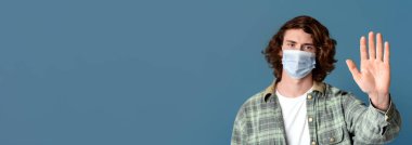 Milenyum adamı tıbbi maske takıyor ve STOP jesti, turkuaz arka plan gösteriyor.