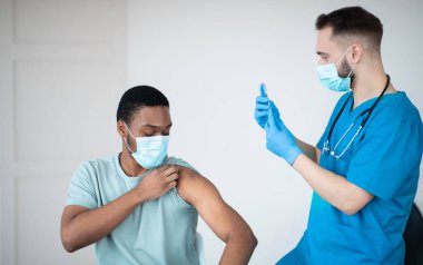Covid-19 aşı programı. Siyah erkek hasta, sağlık merkezindeki doktoru ziyaret ederken koronavirüs aşısı oluyor. Afrikalı Amerikalı adam küresel virüse karşı aşılanıyor