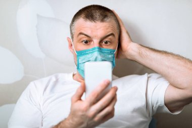 Coronavirus anksiyetesi. Koruyucu Maskeli Korkak Adam evde oturan salgınla ilgili şok edici haberler okuyor. Seçici Odaklanma
