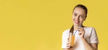 Sarı arka plan üzerinde bir bardak portakal suyu olan güzel bir genç kadın portresi.