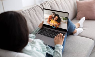 Bir kadın, mutlu bir çiftle görüntülü konuşma yapmak için koltuğuna rahatça oturur. Yumuşak doğal ışık odayı dolduruyor, sohbet için sıcak bir atmosfer yaratıyor..