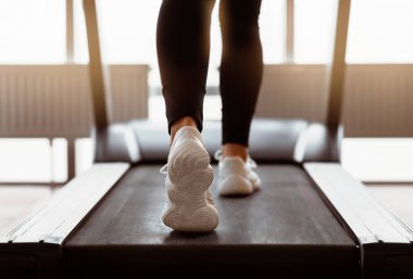 Kardiyo çalışması. Genç bir kadın spor salonunda koşu bandı kullanıyor.