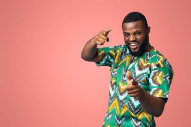 Renkli Afrikalı kostümlü oyuncu siyahi bir genç. Mavi stüdyo arka planındaki kameraya boş alanı gösteriyor. Mutlu Afro-Amerikan karizmatik adam geleneksel parlak kıyafetler sergiliyor.