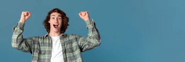 Başarı ve kutlama konsepti. Başarılı genç adam turkuaz arka planda zafer jesti gösteriyor.