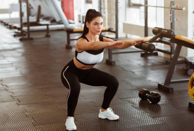 Güçlendirme egzersizleri. Spor kulübünde çömelme yapan genç bir kadın.