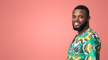 Afro-geleneksel tişörtlü pozitif siyahi adam mavi stüdyo arka planında kameraya bakıyor, kopya alanı olan bir panorama. Neşeli Afrikalı Amerikalı adam mesaj ya da reklam için boş alanın yanında kalıyor.