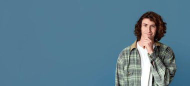 Turkuaz arka planda gülümseyen ve çenesine dokunan neşeli genç adam.