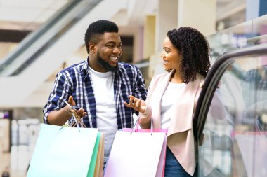 Mağazada yürüyen merdivene binerken neşeli siyahi çift sohbeti, Afro-amerikan erkek Ans kadın enjoyng alışverişi, yeni alışverişleri tartışması. Bir sürü alışveriş torbası, boş alan.