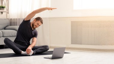 Karantina sporu. Genç adam bilgisayarında online eğitimle spor yapıyor, boş yer var.