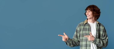 Gülümseyen genç tasarımınız için boş alanı işaret ediyor, turkuaz arka plan. Panorama