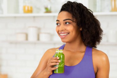 Detox konsepti. Elinde ev yapımı yeşil meyve suyu olan siyah bir kızın portresi. Boş alana bakıyor.