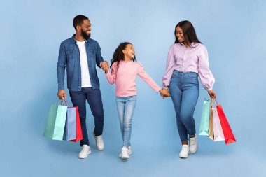 Alışverişe. Üç kişilik neşeli aile boyu alışveriş merkezinden gelen renkli alışveriş torbalarıyla birlikte yürüyorlar. Kız ailesiyle el ele tutuşuyor ve konuşuyor. Turkuaz stüdyo arka planında izole edilmiş bir şekilde.