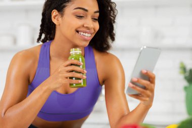 İçkinin tadını çıkarıyorum. Kırmızı spor sutyen giyen siyah bir kız cep telefonu kullanıyor, kahvaltıda ev yapımı sebze suyu tutuyor.