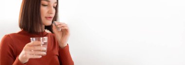 Şık saçlı genç bir kadın temiz bardaktan bir yudum su alır. Rahat ve düşünceli görünüyor, sıcak evinde sakin bir öğleden sonranın tadını çıkarıyor..