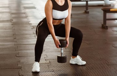 Fitness konsepti. Dambılı genç bir kadın spor salonunda çömeliyor.
