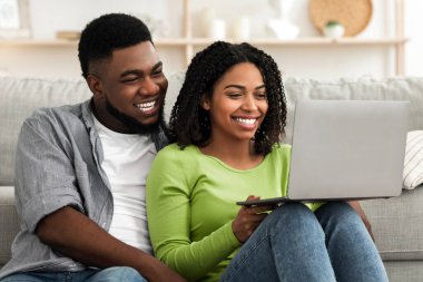 Milenyum siyahi çifti evde dizüstü bilgisayarla dinleniyor, oturma odasında otururken film izliyor ya da internette geziniyor.