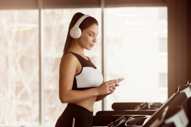Akıllı telefon ve kulaklıklı güzel bayan koşu bandında müzik dinliyor, boşluğu kopyalıyor.