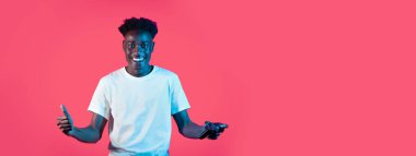 Beyaz tişörtlü neşeli bir genç adam, rahat bir atmosferde parlak pembe bir arka planla çevrili bir oyun kumandasını tutarken heyecanını ifade ediyor..