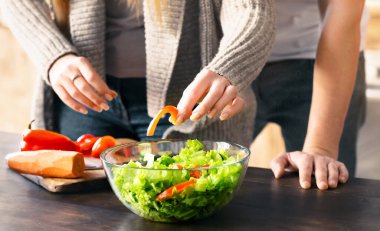 Tanımlanamayan erkek ve kadın mutfakta birlikte sağlıklı salata pişiriyor, el ele tutuşuyorlar.