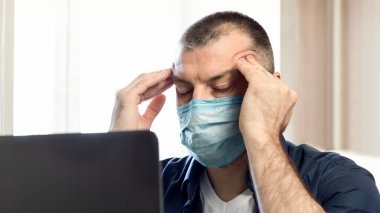 Coronavirus ve Coronacrisis. Dizüstü bilgisayardaki stresli adam tapınaklara masaj yapıyor. Evde iş sorunları yaşıyor. Seçici Odaklanma