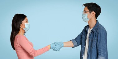 Coronavirus yayılmasının önlenmesi. Genç Koreli adam ve maskeli kız el sıkışıyorlar, birbirlerini selamlıyorlar.