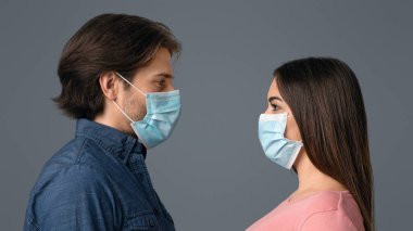 Coronavirus 'a karşı birlikte. Koruyucu tıp maskeli genç bir çiftin portresi. Arka planda ayakta dikilirken birbirlerine bakıyorlar.