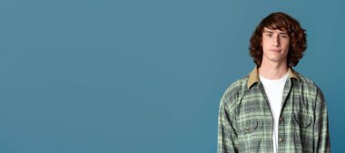 Turkuaz arka planda günlük giysiler içinde ciddi bir genç adam.