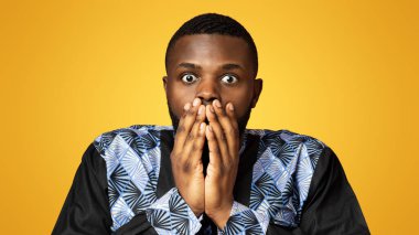 Geleneksel kostümlü afro-amerikan adam ağzını elleriyle kapatıyor, pembe stüdyo geçmişi var. Afrikalı kostümlü, nefes kesici bir şey gören afallamış siyahi adamın yakın çekimi.