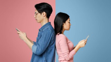 Asyalı kız ve erkek sırt sırta verip karantina sırasında cep telefonu kullanıyorlar.