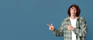 Turkuaz stüdyo arka planında boş bir yeri işaret eden şaşırmış genç adam.